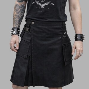 Peut inclure: Débardeur noir avec imprimé graphique et kilt noir à poches. Le haut présente un motif avec des chauves-souris, une croix et un pentagramme. Le kilt a un design plissé et plusieurs poches. La personne porte des bracelets.