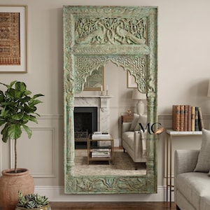 May include: A large, rectangular mirror with a carved wooden frame, painted in a distressed, muted green. The frame features detailed carvings of birds and floral designs. The mirror is a decorative home decor item, suitable for any room.