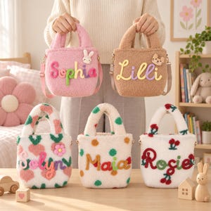 Puede incluir: Cinco bolsos de peluche suaves con asas y correas para el hombro. Dos bolsos son de colores sólidos, rosa con un conejo y beige con un gato. Tres bolsos son blancos con patrones: corazones rosas y una flor, puntos verdes y naranjas, y cerezas rojas.