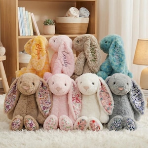 Può includere: Una collezione di coniglietti di peluche in vari colori, tra cui giallo, rosa, marrone, blu, bianco e grigio. Alcuni coniglietti hanno orecchie e piedi con motivi floreali. Diversi coniglietti hanno nomi ricamati sulle orecchie. Un orsacchiotto è seduto su uno sgabello di legno.