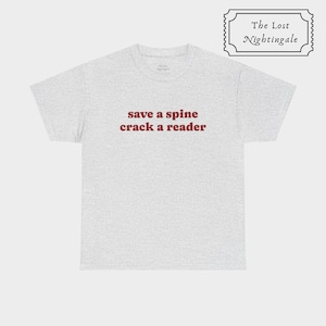 May include: A light gray short-sleeve t-shirt featuring the text "save a spine crack a reader" printed in dark red letters across the chest. The shirt has a crew neckline and a standard fit, with a small logo tag visible inside the collar area.