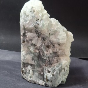 May include: A raw, natural crystal formation with a mix of white, gray, and black hues. The crystal has a rough, textured surface with multiple facets and a crystalline structure. The overall shape is irregular and organic.