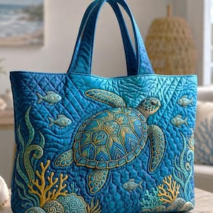 May include: A blue quilted tote bag featuring an embroidered sea turtle, fish, and coral. The design incorporates shades of blue, green, and gold. The bag has a quilted pattern and solid blue handles. The overall theme is marine life.