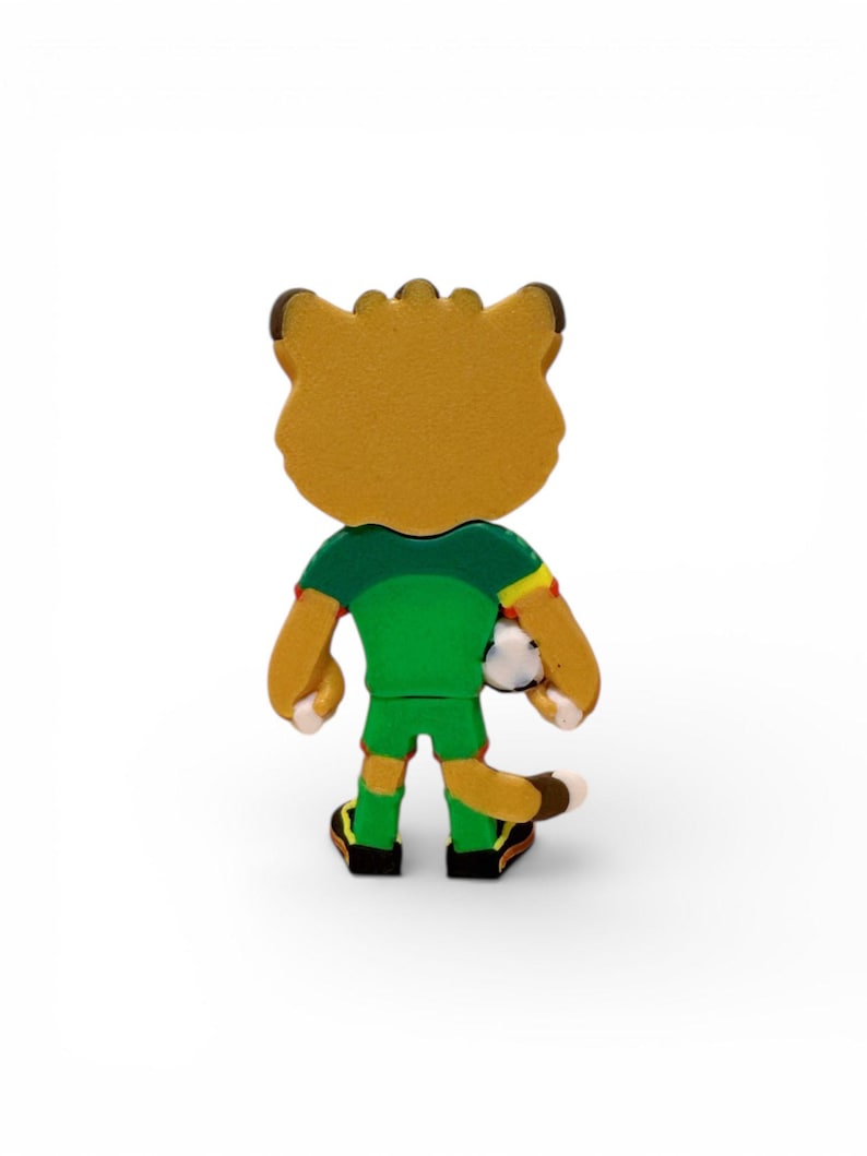 Puede incluir: Figura de un le&oacute;n de dibujos animados con un uniforme de f&uacute;tbol verde, sosteniendo un bal&oacute;n de f&uacute;tbol. El le&oacute;n tiene un cuerpo marr&oacute;n, orejas marrones y zapatos negros y amarillos. Vista trasera.