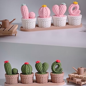 May include: A collection of decorative cactus sculptures in white and brown pots on a wooden tray. The cacti are pink and green, with some shaped like the letters L, O, V, and E. Each cactus has a different flower on top.