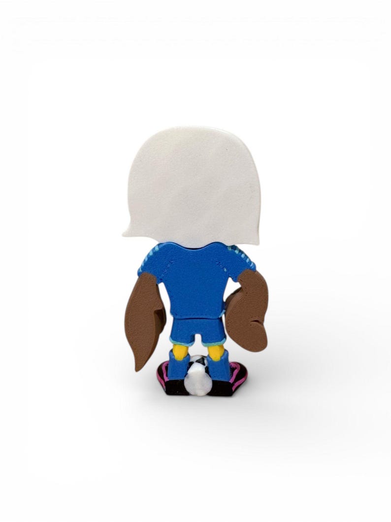 Puede incluir: Una figura de dibujos animados de un futbolista, vista desde atr&aacute;s, en azul, marr&oacute;n y amarillo. La figura tiene una cabeza blanca, una camiseta azul, brazos marrones, pantalones cortos amarillos y zapatos negros y rosas. Un bal&oacute;n de f&uacute;tbol est&aacute; a los pies.
