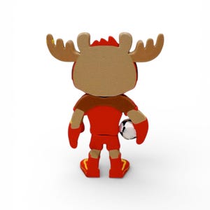 Puede incluir: Una figura de dibujos animados de un alce con uniforme de f&uacute;tbol rojo, sosteniendo un bal&oacute;n de f&uacute;tbol. El alce tiene cuernos marrones y un cuerpo rojo y marr&oacute;n. La figura est&aacute; sobre una superficie blanca.