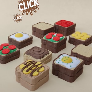 Op de afbeelding: Een verzameling miniatuurvoedselartikelen die toast met verschillende toppings voorstellen. De toppings zijn onder meer een gebakken ei, plakjes tomaat, chocoladepasta en gele fruitschijfjes. Het woord "CLICK" is in een bruin lettertype geschreven.