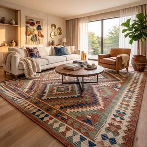 May include: A living room with a patterned rug in red, blue, and green. A white sofa with cushions and a brown leather armchair surround a round coffee table. A large potted plant is near a window. The room has a neutral colour scheme.