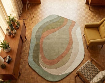 May include: An abstract area rug with a unique shape and a layered design. The rug features soft, muted colors including shades of green, peach, and beige. The rug is placed on a wooden floor, creating a warm and inviting atmosphere.