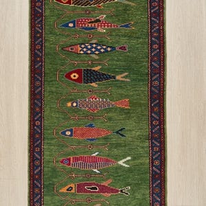May include: A rectangular green rug with a repeating pattern of colorful fish. The fish are in various colors, including red, blue, and brown, and are arranged vertically. The rug has a dark blue border with a repeating geometric pattern.
