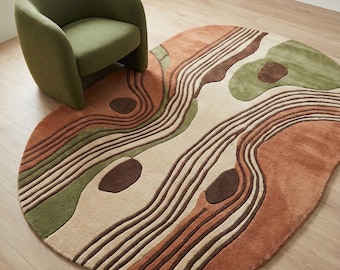 May include: An abstract, oval-shaped rug with a landscape design in shades of brown, beige, and green. The rug features a series of curved lines and organic shapes, creating a textured appearance. A green armchair sits nearby, complementing the rug's color palette.