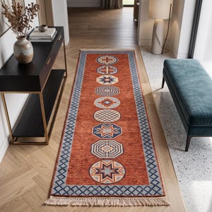 May include: A long rectangular runner rug in a deep burnt orange color featuring a central vertical row of nine distinct geometric circular motifs in shades of blue, cream, and brown, framed by a blue diamond border and finished with fringe.