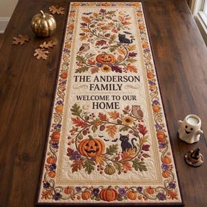 Peut inclure: Un chemin de table rectangulaire en tissu avec un fond crème orné de motifs automnaux brodés, notamment des citrouilles orange, des hiboux bruns, des chats noirs et des feuilles d'automne. Le texte indique THE ANDERSON FAMILY WELCOME TO OUR HOME.