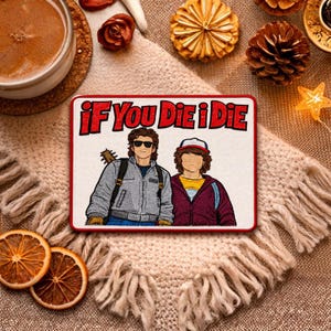 May include: Embroidered patch featuring two cartoon characters with the text "If You Die I Die" in red and white. The patch is rectangular with a red border and is set on a beige fringed surface.