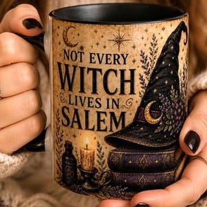 May include: A ceramic mug with a black interior and handle, featuring a beige background with the text "NOT EVERY WITCH LIVES IN SALEM". The design includes a black pointed hat, stacked books, a lit candle, and a small bottle with a star symbol.