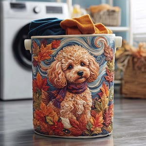 May include: A cylindrical laundry hamper featuring a textured relief illustration of a curly-haired golden dog wearing a purple scarf, surrounded by vibrant orange, red, and yellow autumn leaves against a swirling blue background.