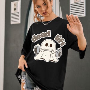 May include: Black t-shirt with a graphic of a cartoon ghost lifting weights. The text "dead lift" is above and to the right of the ghost. The ghost is white with a smiling face. The shirt has short sleeves.