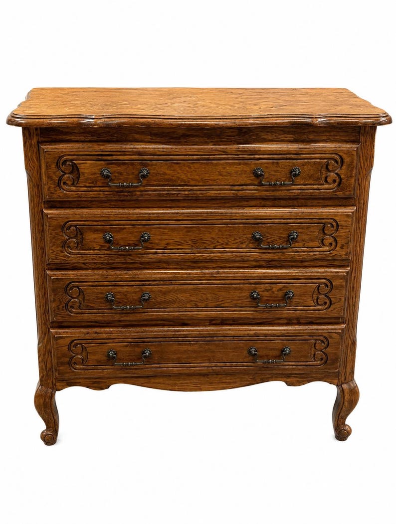 May include: A medium brown wooden chest of drawers featuring four horizontal drawers with carved scrollwork detailing on the drawer fronts. The piece stands on four curved cabriole legs and includes dark metal hardware pulls on each drawer.