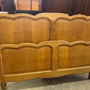 May include: A light brown wooden bed frame. The headboard and footboard feature a decorative, curved design. The frame is made of solid wood and has a classic, vintage style, suitable for a double bed.