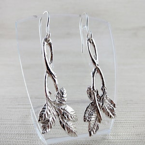 May include: Silver dangle earrings with a twisted stem design and leaf accents.