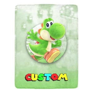 Op de afbeelding: Een groene pluche deken met een Yoshi-cartoonfiguur in een cirkelvormig ontwerp. Het personage is groen met een witte buik, oranje schoenen en een rood zadel. Het woord "CUSTOM" staat in kleurrijke letters onderaan.