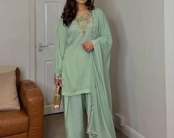 Op de afbeelding: Een mintgroene salwar kameez set. De top heeft ingewikkelde borduursels rond de halslijn en manchetten. De set bevat een broek met wijde pijpen en een bijpassende dupatta. Een gouden clutch en versierde hakken maken de look compleet.
