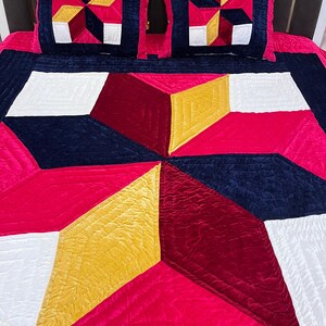 Può includere: Un copriletto e due federe con un motivo geometrico. Il design utilizza tessuto di velluto rosso, bianco, giallo e blu navy. Il copriletto e le federe hanno una texture trapuntata.