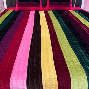 May include: A vibrant bed set featuring a striped design in various colors, including pink, yellow, green, and burgundy. The set includes a comforter and two matching pillows with a striped pattern. The bed set is made of a soft, plush material.
