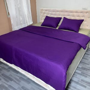Puede incluir: Una cama con una colcha morada y dos almohadas moradas a juego. El cabecero es de color beige claro con un patrón de diamantes. La cama está hecha y lista para usar.
