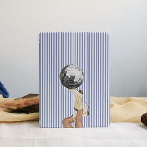 Puede incluir: Una funda para tableta con un fondo a rayas azules y blancas. La funda presenta una ilustración de una bola de discoteca equilibrada sobre un par de botas de vaquero. Las botas son de color beige y blanco.