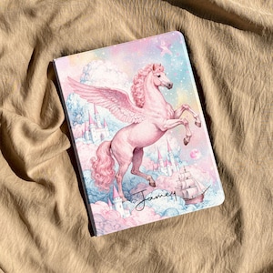 Puede incluir: Una funda rectangular para tableta con un pegaso rosa encabritado entre nubes pastel, estrellas y castillos. Un barco de vela es visible en la esquina inferior derecha. El nombre Jamey está impreso en cursiva negra en la parte inferior.