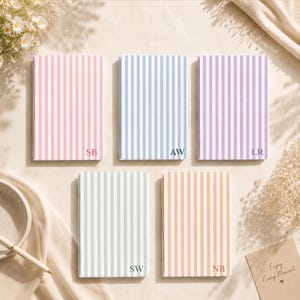 May include: Five rectangular notebooks with vertical stripes in pastel pink, blue, purple, mint green, and peach. Each notebook features two-letter initials printed in the bottom right corner: SB, AW, LR, SW, and NB respectively.