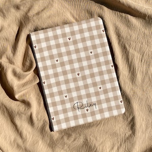 May include: A rectangular tablet case featuring a beige and white gingham check pattern with small brown hearts scattered across the surface. The name Riley is printed in a black cursive script font near the bottom center of the cover.