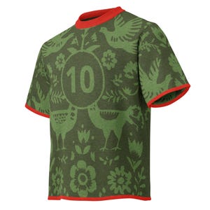 May include: Olive green t-shirt with a repeating pattern of birds, flowers, and foliage in a lighter green hue. The number "10" is centered on the front. The collar and sleeve edges are trimmed with red.