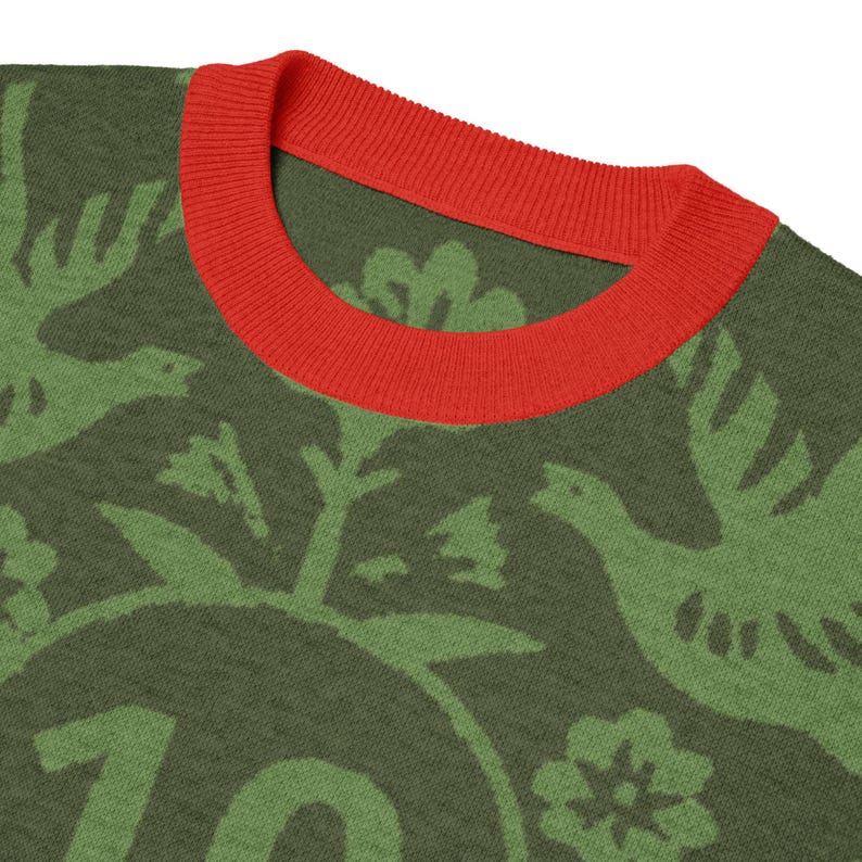 May include: Close-up of a green sweater with a red ribbed neckline. The sweater features a repeating pattern of green birds, flowers, and foliage. The number 70 is visible in the lower portion of the sweater.