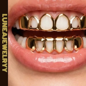 May include: Close-up of a person's mouth with gold teeth grillz. The grillz cover the top and bottom teeth, with a shiny, reflective surface. The text "LUNEAJEWELRYY" is vertically aligned on the left side of the image.
