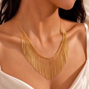 May include: A gold-toned necklace featuring a multi-layered fringe design composed of numerous thin, vertical metallic strands suspended from a delicate chain. The piece rests against the collarbone, creating a cascading effect with its uniform, slender, and polished gold-coloured metal rods.