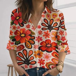 May include: A long-sleeve button-down shirt featuring a cream base with a vibrant, repeating floral pattern in shades of red, orange, yellow, and pink. The shirt has a classic collar, a front button placket, and cuffs on the sleeves.