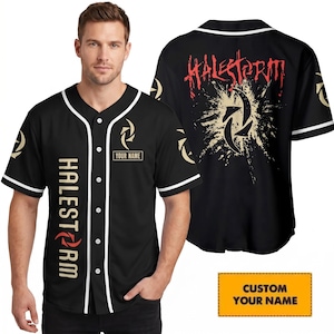 May include: A black baseball jersey with white piping, featuring the text HALESTORM in gold and red on the front, a custom name box, and a large red and gold graphic on the back. The shirt has short sleeves and a button-down front closure.