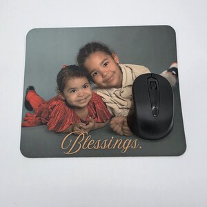 Könnte beinhalten: Ein rechteckiges Mauspad mit einem Foto von zwei Kindern und dem Wort "Blessings" in Schreibschrift. Eine schwarze kabellose Maus liegt auf dem Pad. Die Kinder lächeln.