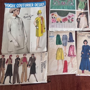 Könnte beinhalten: Eine Sammlung von fünf Vintage-Vogue-Schnittmusterumschlägen mit verschiedenen Kleidungsillustrationen, darunter Mäntel, Röcke, Kleider und Oberteile mit Stickmustern. Die Papierumschläge zeigen gedruckten Text wie Vogue Couturier Design, Focus on Embroidery und verschiedene Schnittmusternummern.
