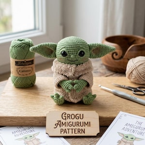 Può includere: Una bambola amigurumi Grogu all'uncinetto, verde e beige, con grandi orecchie e occhi neri, è esposta su una superficie di legno. Un cartello di legno recita "Grogu Amigurumi Pattern". Sono visibili anche un gomitolo di filo verde e un uncinetto.