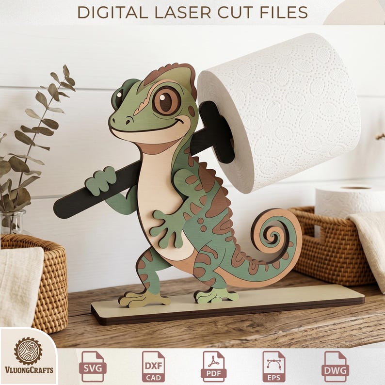 May include: A laser-cut wooden toilet paper holder shaped like a cartoon chameleon, holding a black bar that supports a roll of white toilet paper. The chameleon is green, brown, and beige, with the text "DIGITAL LASER CUT FILES" at the top.