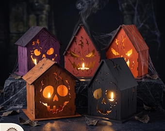 May include: Five wooden house-shaped lanterns with laser-cut skull and jack-o'-lantern faces, illuminated from within by tea lights. The structures are stained in purple, orange, and black, featuring cutouts of spiderwebs and cracks.