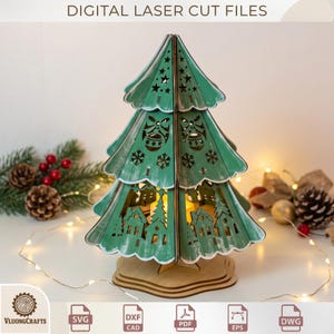 Peut inclure: Une décoration de sapin de Noël en bois découpé au laser de couleur verte, présentant des découpes complexes d'étoiles, de cloches, de flocons de neige et d'un village. La structure est éclairée de l'intérieur et repose sur une base en bois.