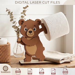 May include: A wooden bear-shaped toilet paper holder. The bear is brown with a lighter brown belly and holds a roll of white toilet paper. The words "DIGITAL LASER CUT FILES" are at the top. The holder is on a wooden base.