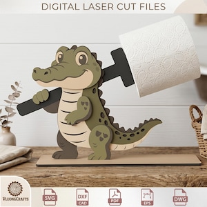 May include: A laser-cut alligator toilet paper holder. The alligator is green and tan with a black bar holding the toilet paper roll. The base is tan. The text "DIGITAL LASER CUT FILES" is at the top.