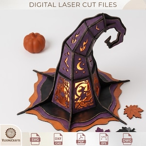 May include: A purple and black laser-cut wooden witch hat decoration featuring cutouts of a witch on a broom, crescent moons, stars, bats, and flames. The structure is illuminated from within and accompanied by a small orange pumpkin and leaf.