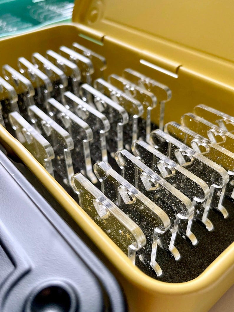 May include: A close-up shot of a yellow container filled with multiple clear, acrylic, comb-shaped objects. The objects are arranged neatly inside the container, which has a black interior. The container is open, revealing the contents.